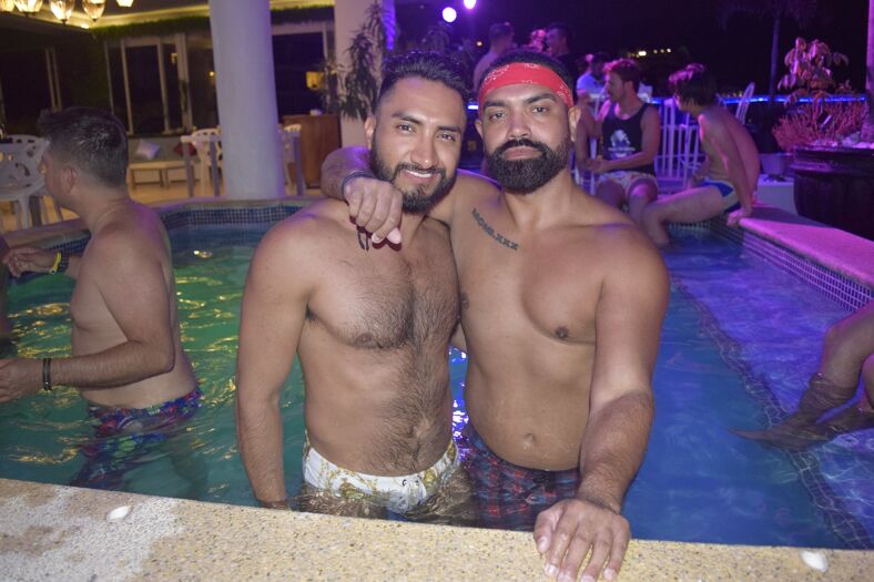 Two shirtless men embracing in a pool at a party.