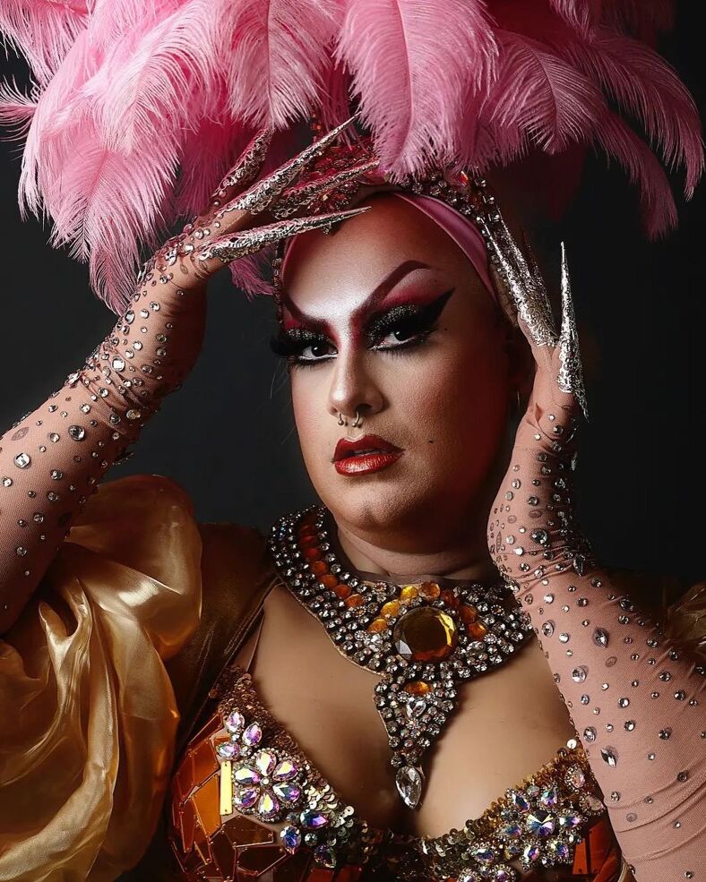Bedazzled drag queen takes a close-up with a giant pink feathered headpiece. 