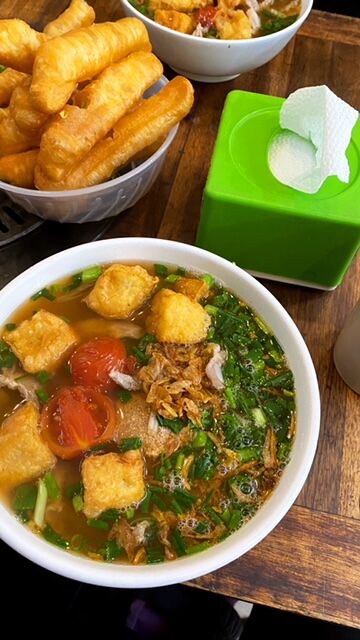 Steaming tofu, tomatoes, and herb soup with a bowl of savory donuts for dipping on the side.