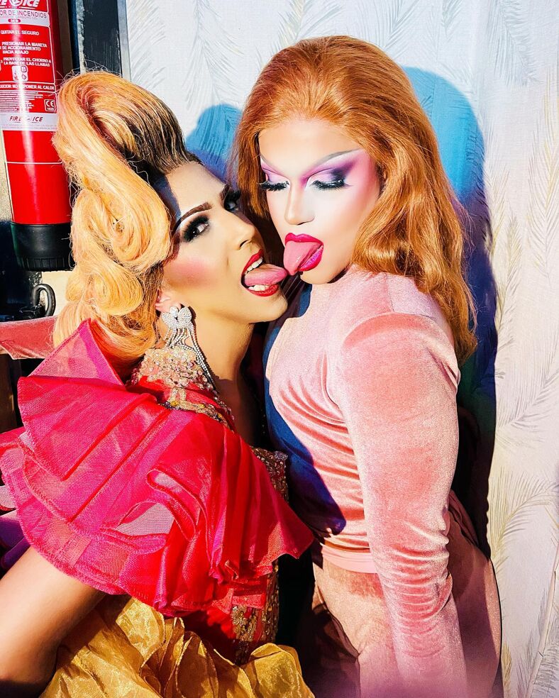 Two fabulous drag queens kiss with their tongues.