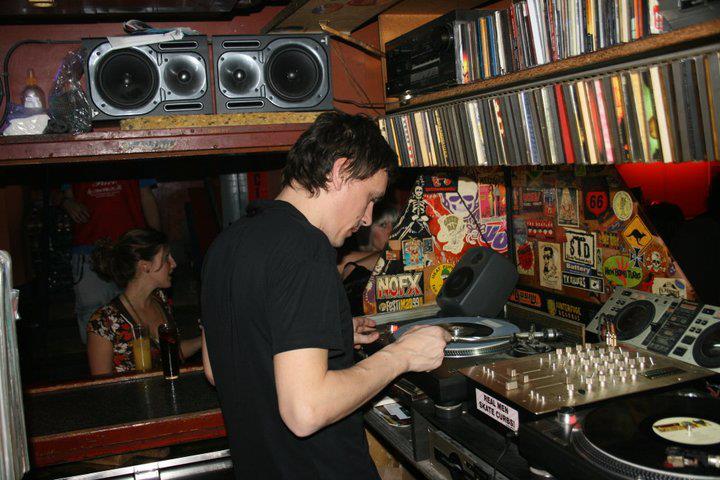 A DJ at La Via Lactea puts the needle on a record while surrounded by a library of music.
