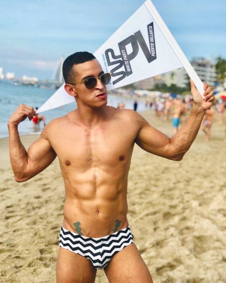 Shirtless man on the beach holding a White Party Puerto Vallarta flag.