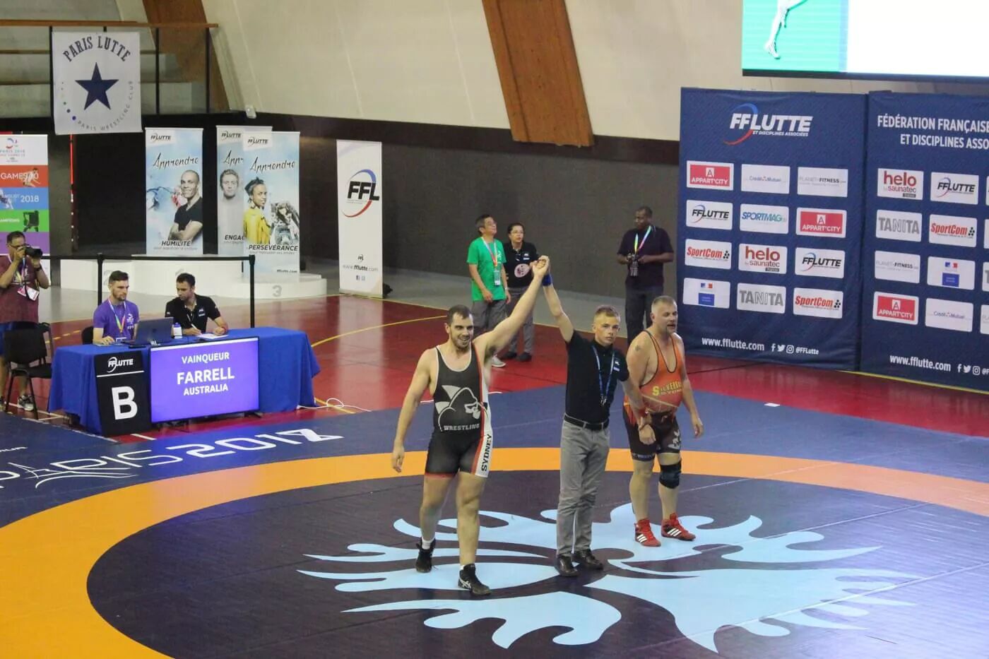 Wrestling referee holds the winner's hand at the end of the match.