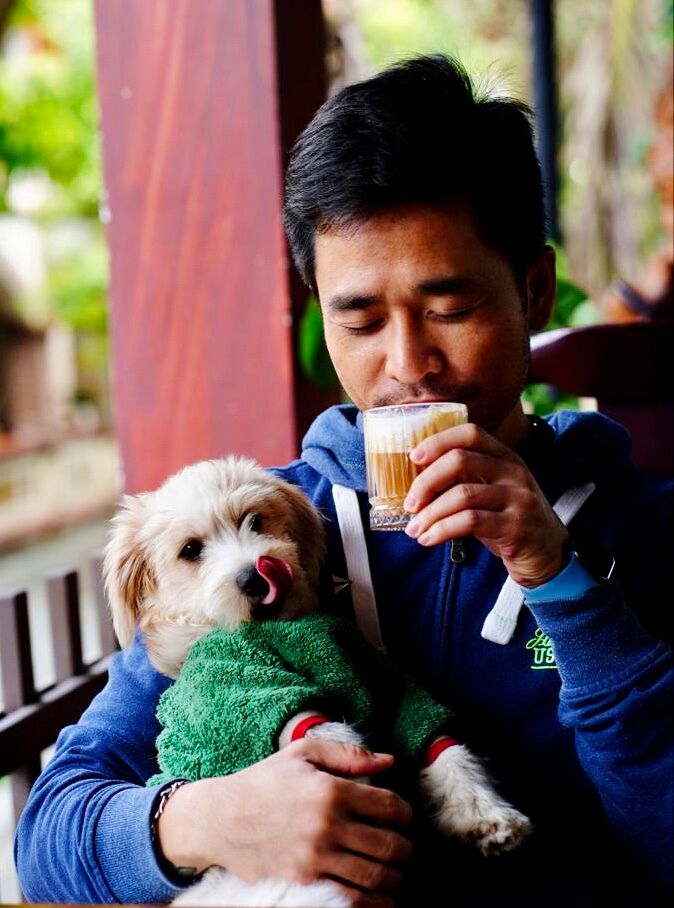 The owner of Cup of Fave coffee and garden cafe drinks a tasty coffee with one hand and holds a cute dog licking its lips in the other.