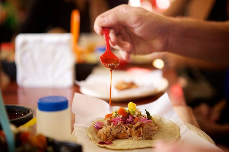 Close up of a hand drizzling sauce onto a taco