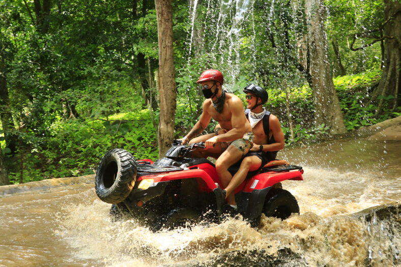 Shirtless men riding through a puddle of water on an ATV.