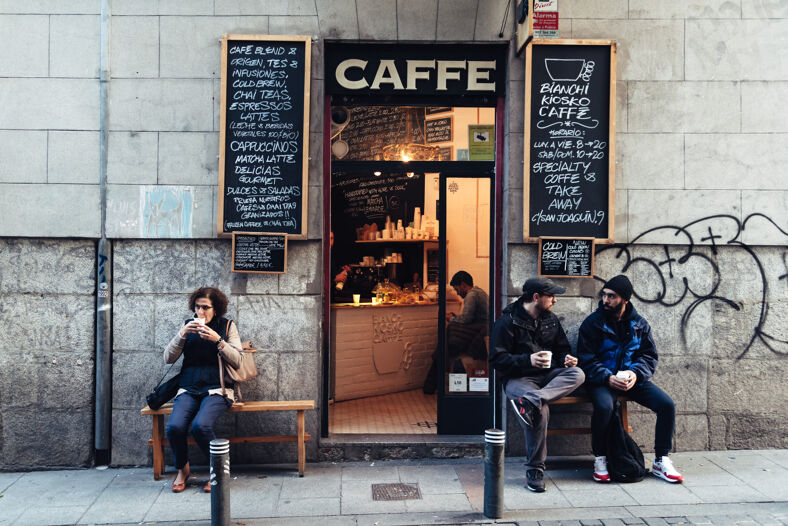 People drinking coffee outside a hole-in-the-wall cafe.