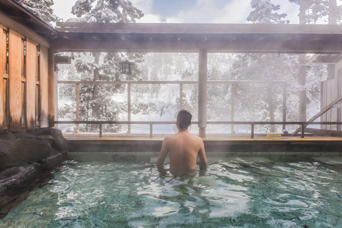 Man soaking in a Japanese Onsen peers into the snowy forest scenery. 