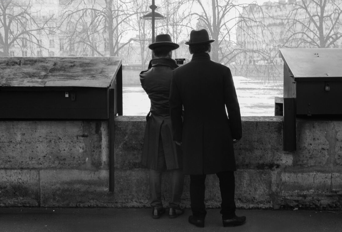 Two men dressed in top hats and trench coats look over a wintery park in Paris France.