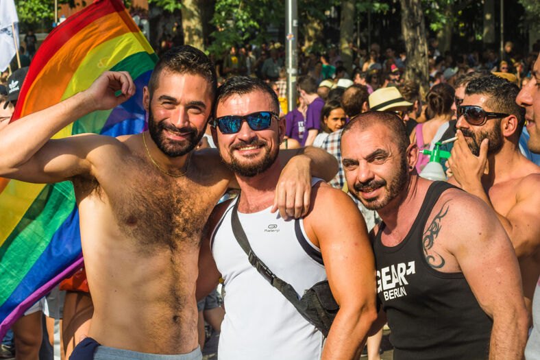 Shirtless men pose in front of a rainbow flag during Madrid pride.