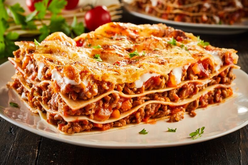A Slice of traditional meat and cheese lasagna on a white dinner plate.