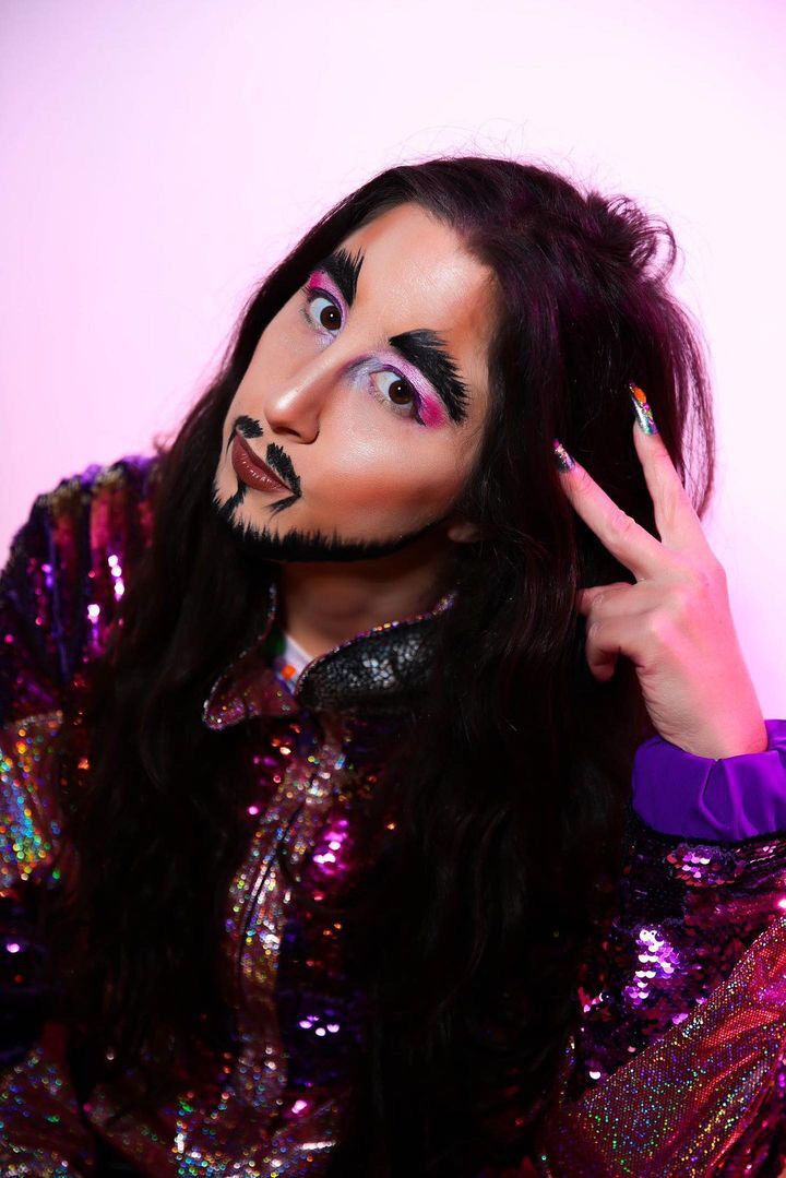 Vera the drag king poses for the camera in facial hair and vibrant pink ye make-up.