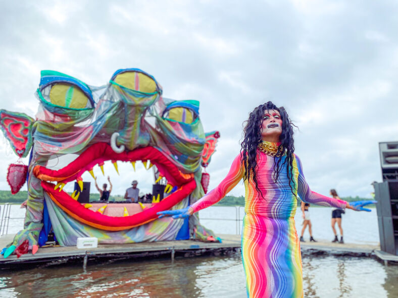 A psychedelic drag performer dances in front of the floating stage monster stage at Whole Queer Festival.