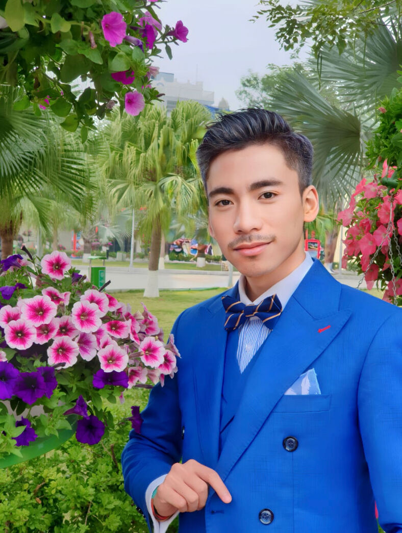 Hiro poses in front of flowers in a blue suit in Hanoi.
