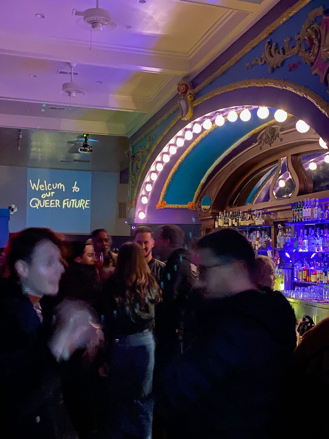 Inside Mother, the ornate mulit-colored bar resembles a cinema marquee. A bouquet of queers mingle under a sign that says "Welcum to our Queer Future"