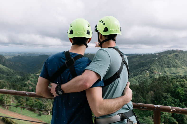 Two men wearing helmets looking at the natural landscape of Puerto Rico from a vista.