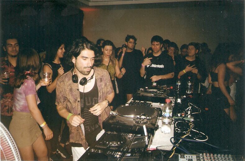 A DJ plays music in the midst of a packed room of people dancing.