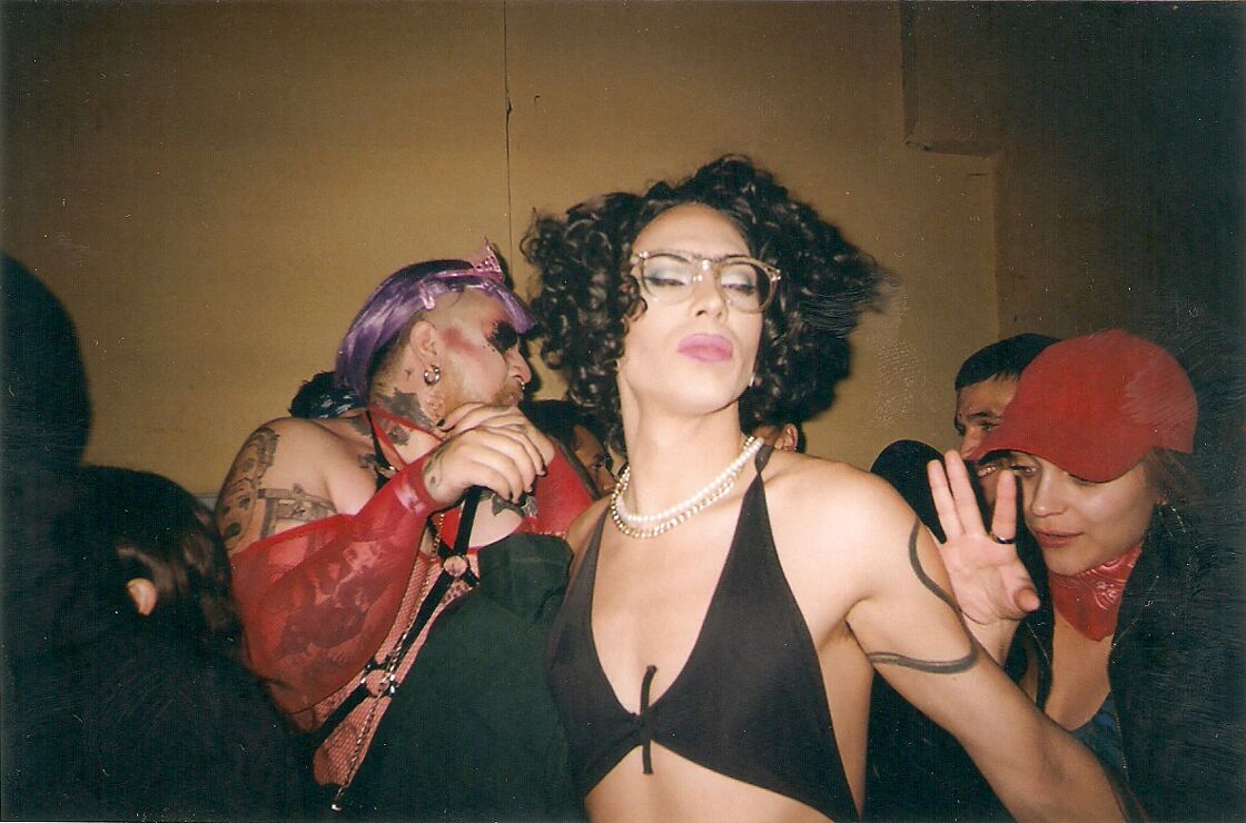 A woman in a black tank top dancers in Santiago amongst people in drag and leather harnesses.