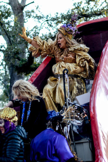 Women of the Muses parade sit in a large float shaped like a high heel shoe.