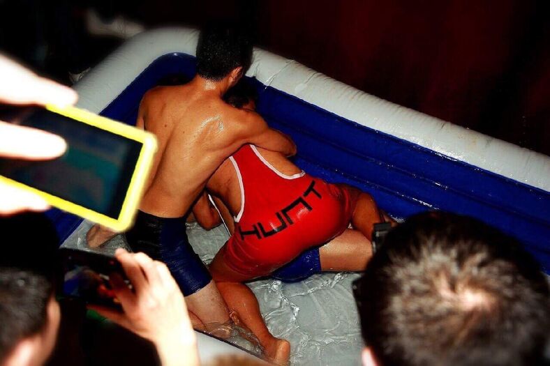 Three men in singlets wrestle in a bathtub full of lube.