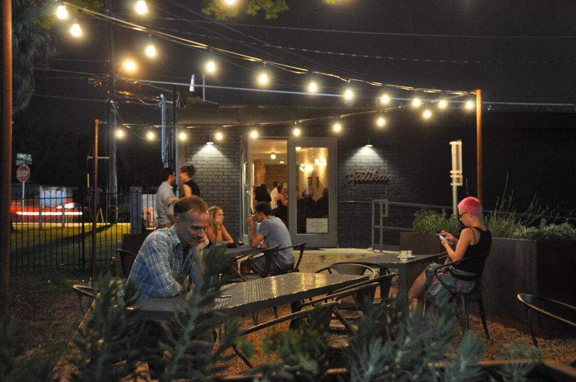 Outdoor patio at night. A few people are chatting and enjoying coffee under bright twinkle lights