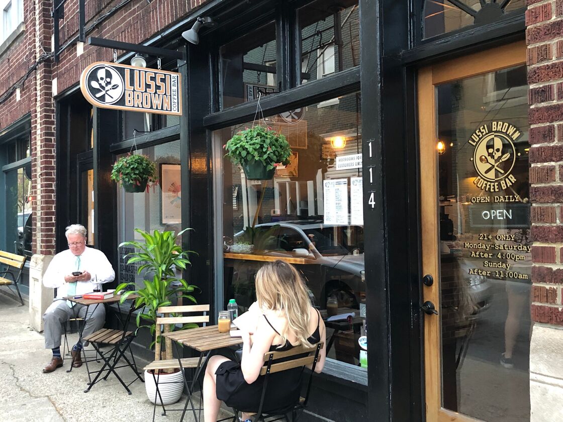 Patrons at Lussi Brown sit outside the cafe in the sun, drink coffee, and unwind while reading a book.