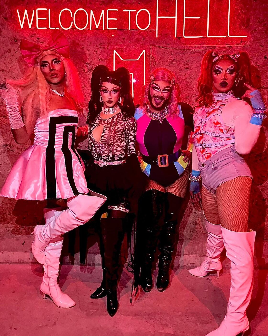 Four sassy drag queens pose in front of a sign that reads "Welcome to Hell" at DIX bar.