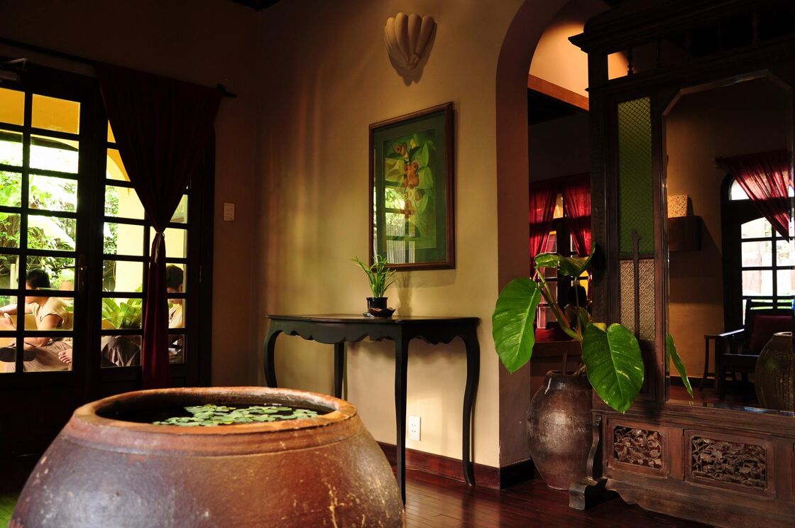 The lobby of NẤM SPA is decorated in ornate wooden decor and giant ceramic containers filled with lush plants. 