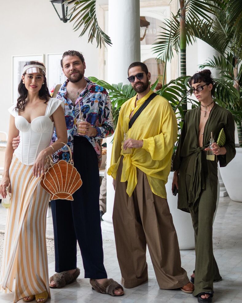 Four stylish men and women pose for the camera dressed in colorfully draped outfits and accessories. 