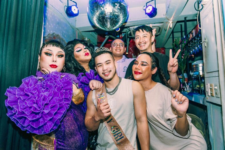 Patrons at Cafe Dalida pose with the night's drag queen who is dressed in a purple ruffled dress.