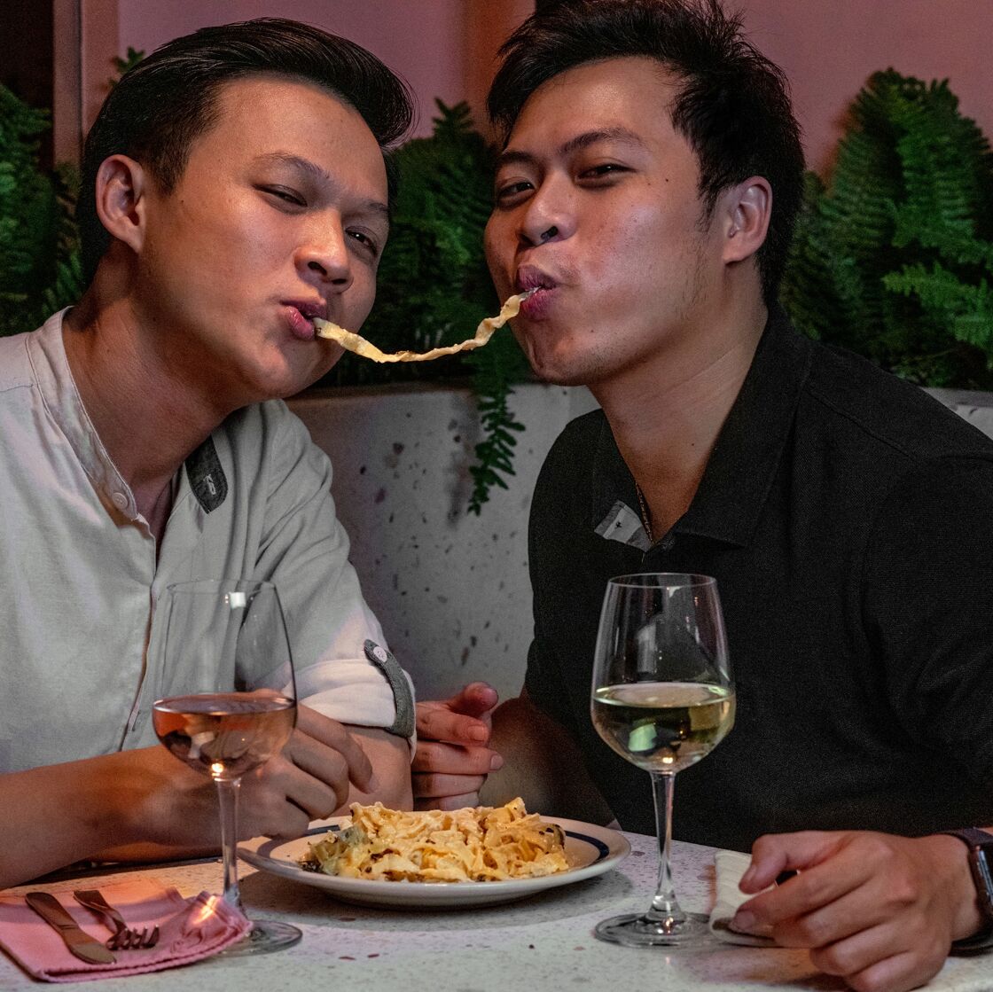 Two cute men slurp a pasta noodle together at Cafe Marcel.
