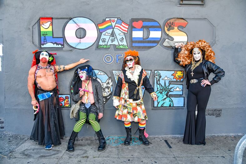 Members of The Sisters of Perpetual Indulgence posing in front of a mural that reads "Loads of Love".
