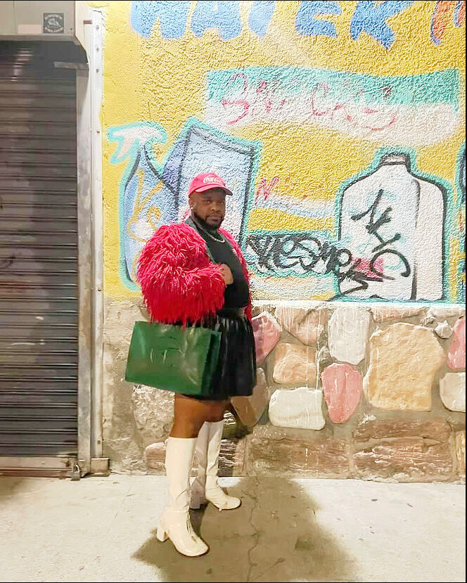 Marco Labeija  poses in front of street art with their green telfer bag and white gogo boots.