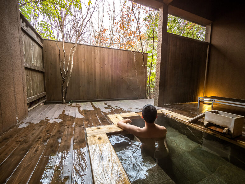 A person soaks in a rustic tub inside a relaxing hot springs.