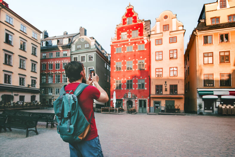 A man wearing a red shirt and a backpack taking a photo with his phone in Stockholm.