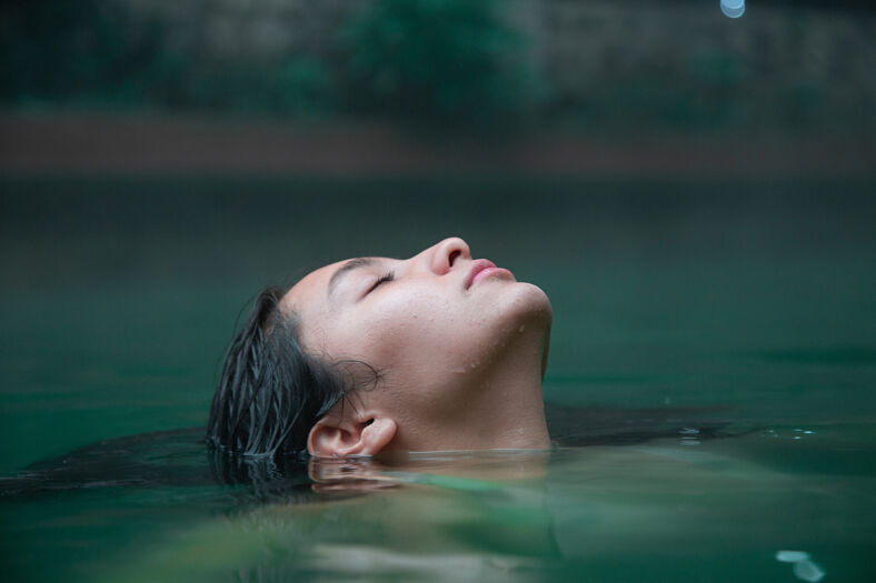 A women with eyes closed soaks in the tranquil waters.