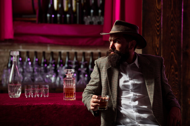 A handsome cowboy drinks whiskey at a western bar.