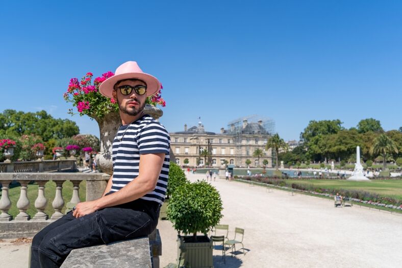 A man in a striped shirt and pink fedora sitting on a ledge in Jardin Luxembourg.