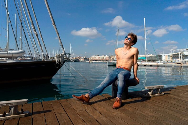 A shirtless man wearing sunglasses sitting on a dock in Valencia.