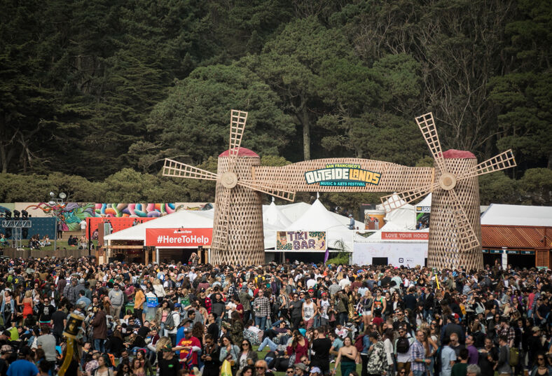 The crowd at Outside Lands in San Francisco's Golden Gate Park under a Dutch windmill marquee that reads "Outside Lands".