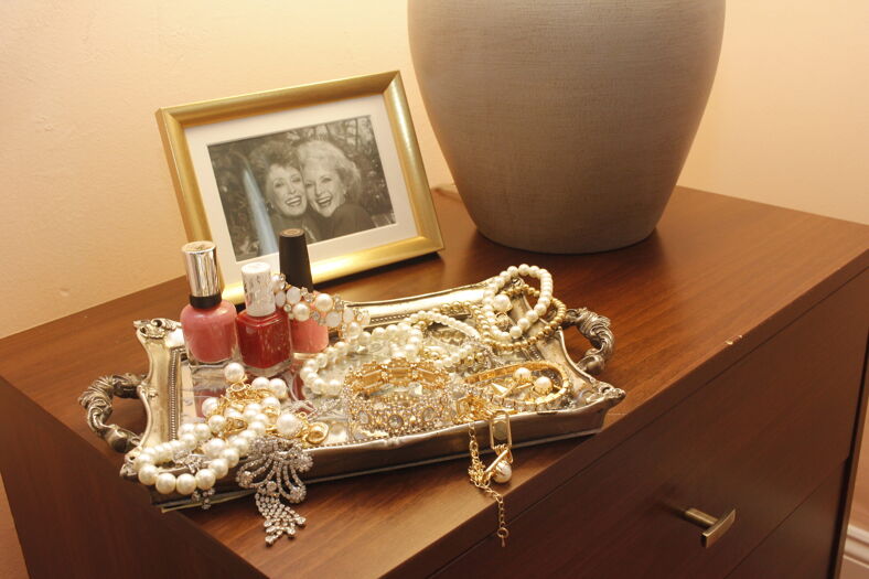 A night stand with jewelry, nail polish, and a framed picture of "Golden Girls" characters.