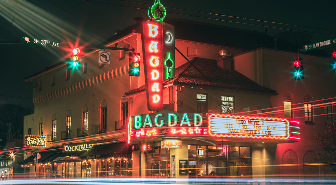 An exterior view of Bagdad Theater and Pub. The building is lit up by several giant neon signs.