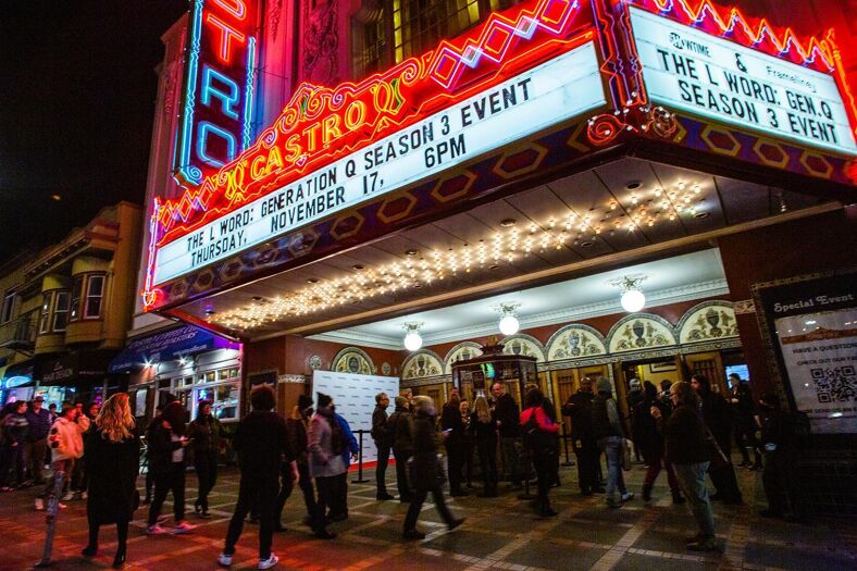 The marquee of the iconic Castro Theatre glows  as people walk by to admire the iconic  building.