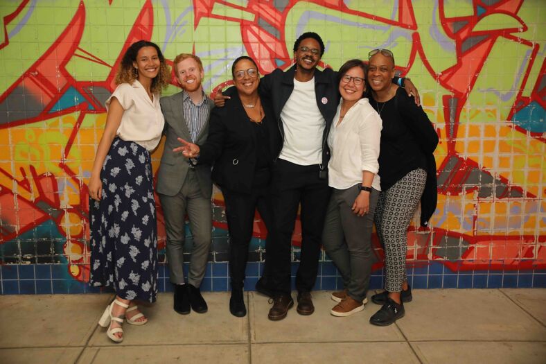 The staff at The DC Center for the LGBT Community smiles at the camera in front of a colorful mural.