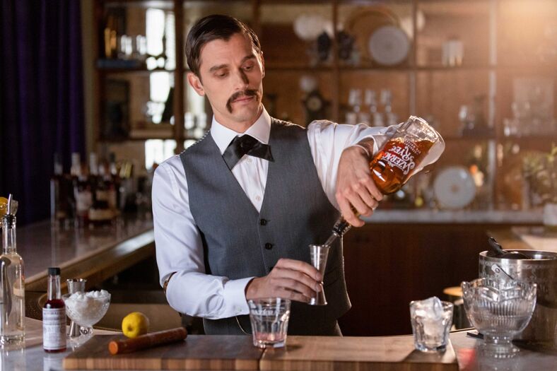 Antoni sports a fake mustache and pours a drink.