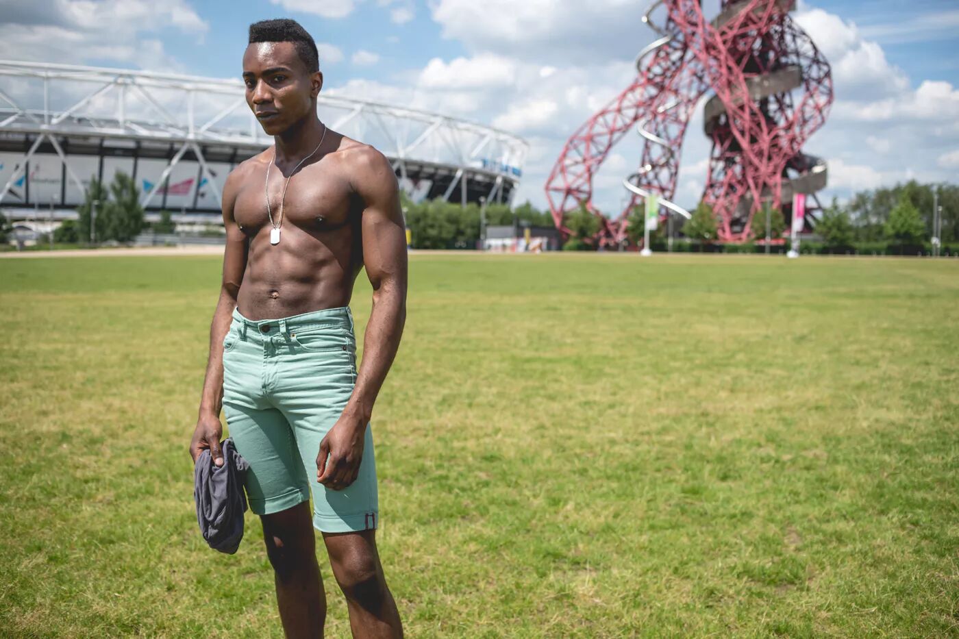 Man posing shirtless in front of Olympic Stadium in London.