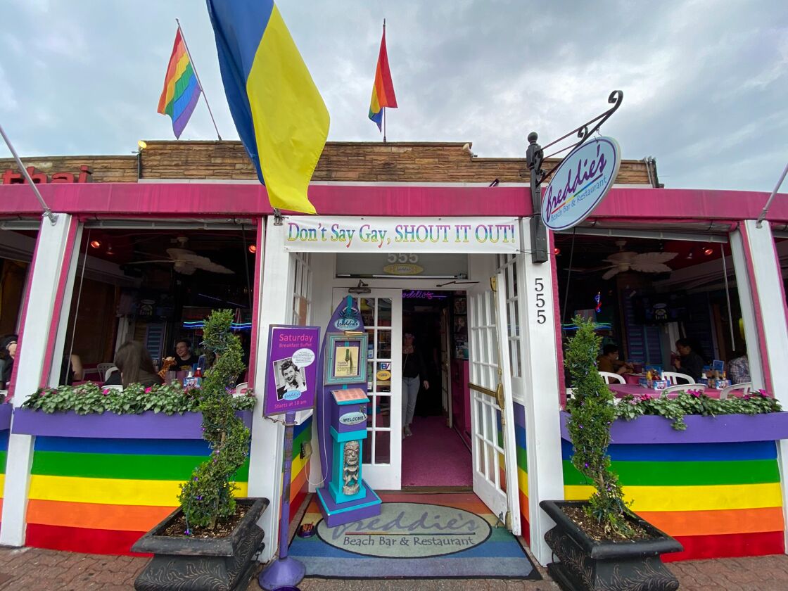 Street view of a gay bar with a sign that reads "Dan't say gay, shout it out!"