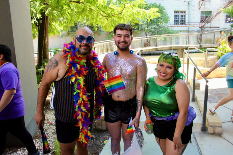 Three people covered in glitter, feathers and fun smile at the camera outside