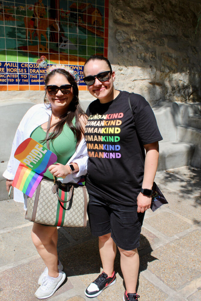 Two women stand in the sun holding pride flags
