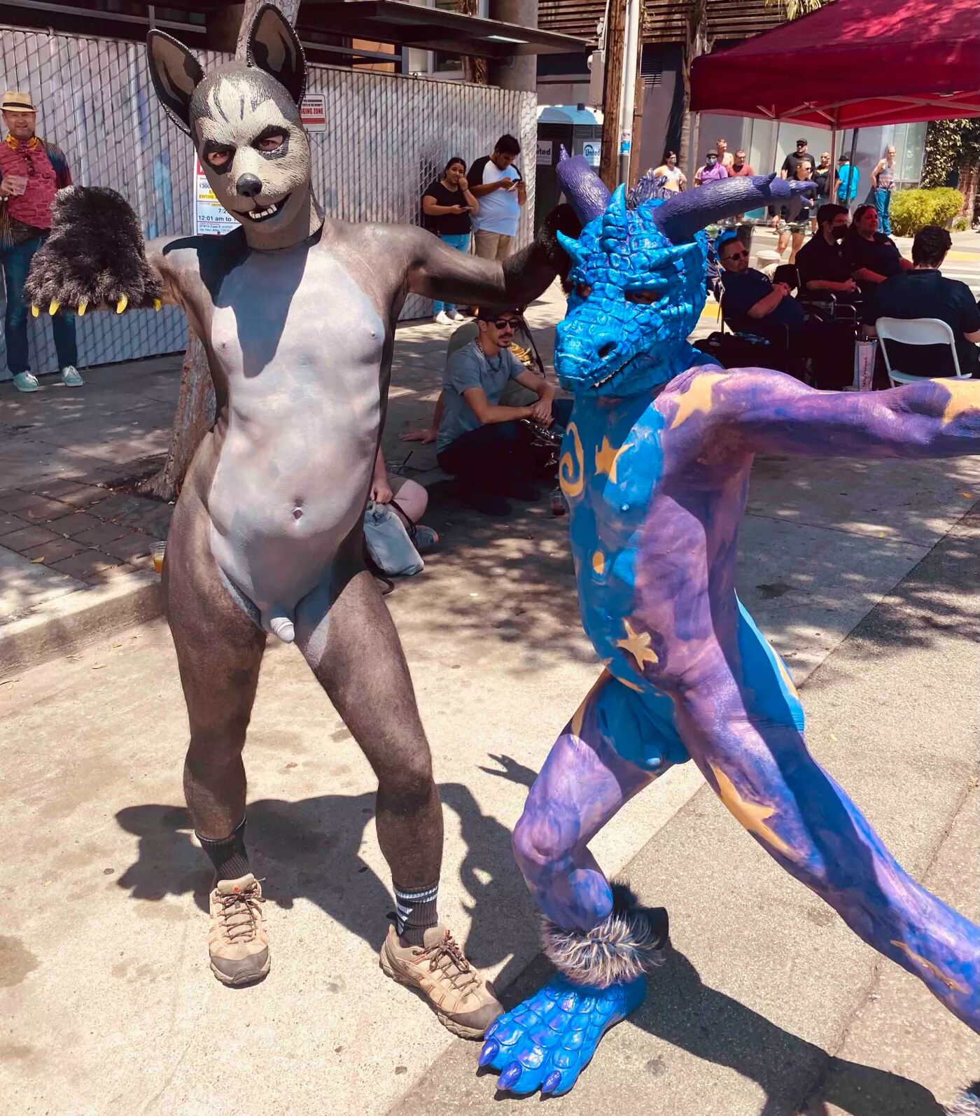Two people wearing animal masks and full body paint strike poses in the street